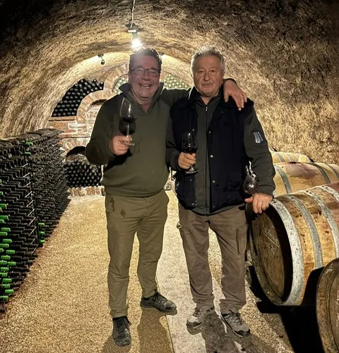 Twee mannen proosten met een glas wijn in de historische kelder, naast eikenhouten vaten